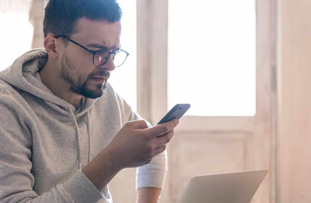Hombre con gafas mira con desconfianza un SMS en el móvil, posible estafa de luz o gas
