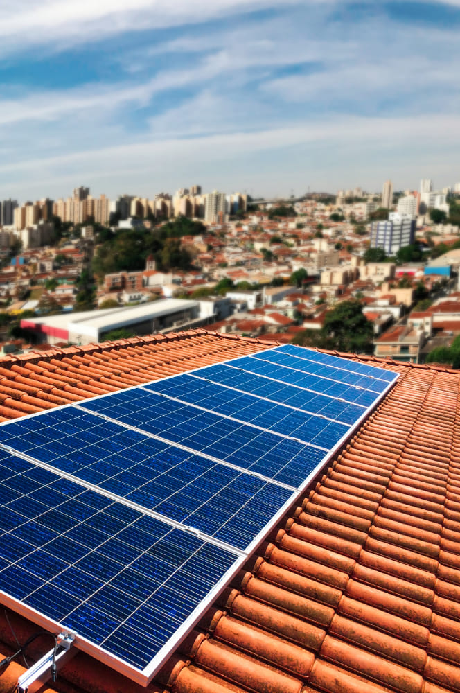 Paneles solares instalados sobre un tejado de tejas rojas en una vivienda residencial, optimizando la eficiencia energética doméstica con vistas a la ciudad.