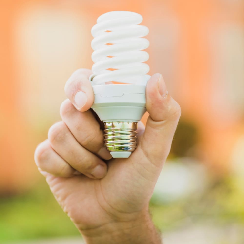 Certificados de Ahorro Energético (CAE) 2 Mano sosteniendo una bombilla de bajo consumo que representa los Certificados de Ahorro Energético CAE